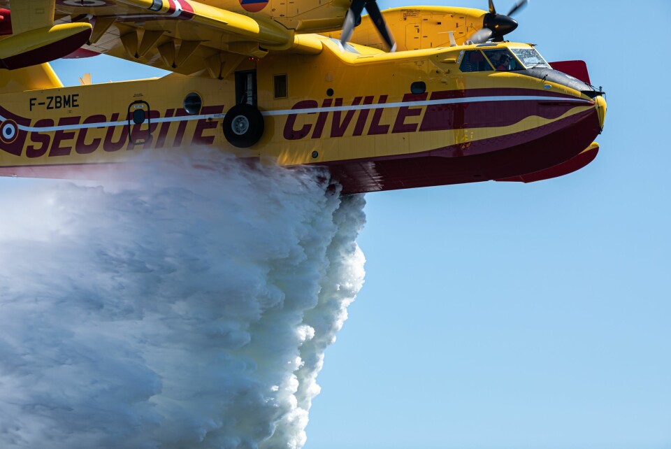 A yellow Bombardier plane dropping water over a forest fire near Bordeaux, France