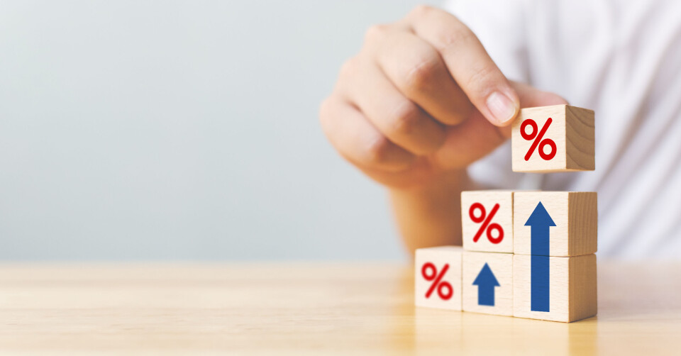 A hand placing a toy block with a % sign on it on a wooden ‘staircase’ to symbolise rising inflation