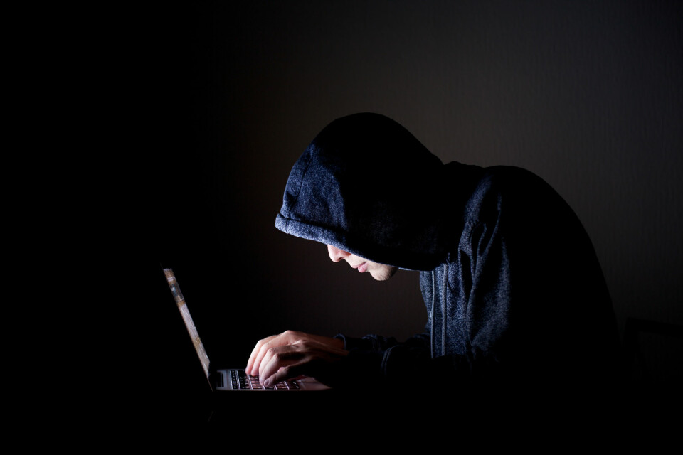 A man in a black hoodie hunched over a laptop
