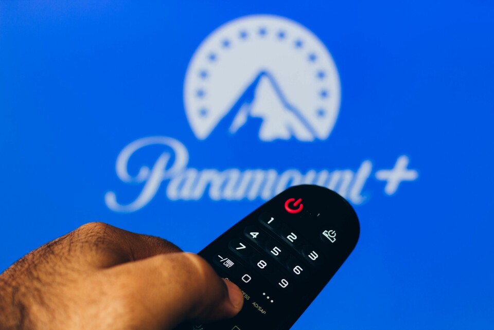 A photo of a TV viewer holding a remote control in front of a TV with the Paramount + screen
