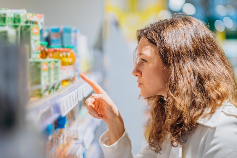 A photo of a woman looking at a food shelf and pointing at a product to study its packaging