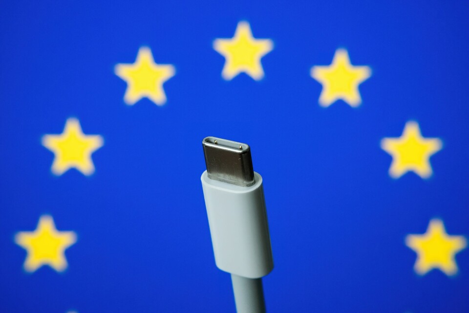 A USB-C charger held up against a background of the European flag