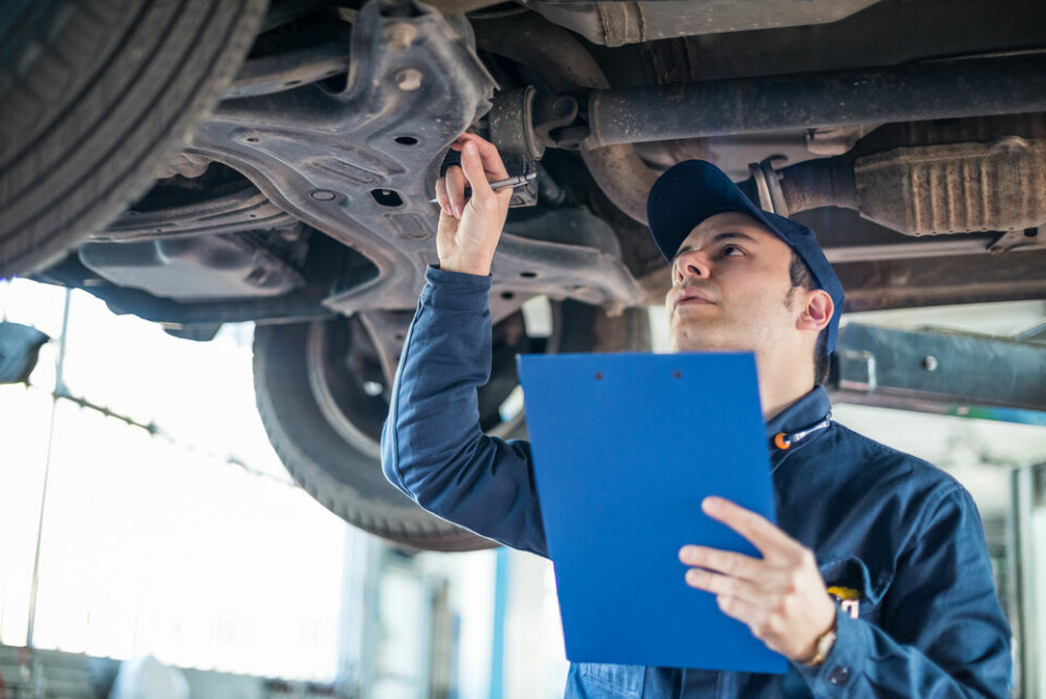 A mechanic holding a clipboard and checking a vehicle in a garage
