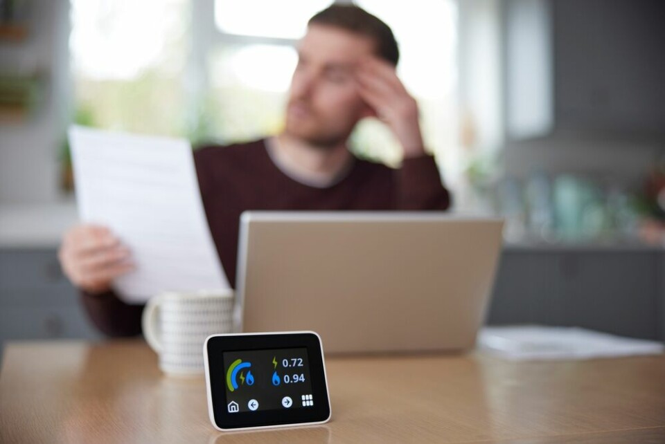 A photo of a man looking at an energy bill with a smart meter in the foreground to show rising costs
