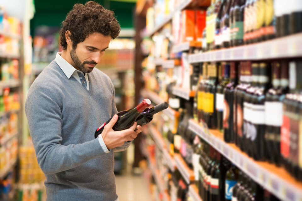 Minerva Studio / Shutterstock An image of a man looking at a bottle of wine in the supermarket