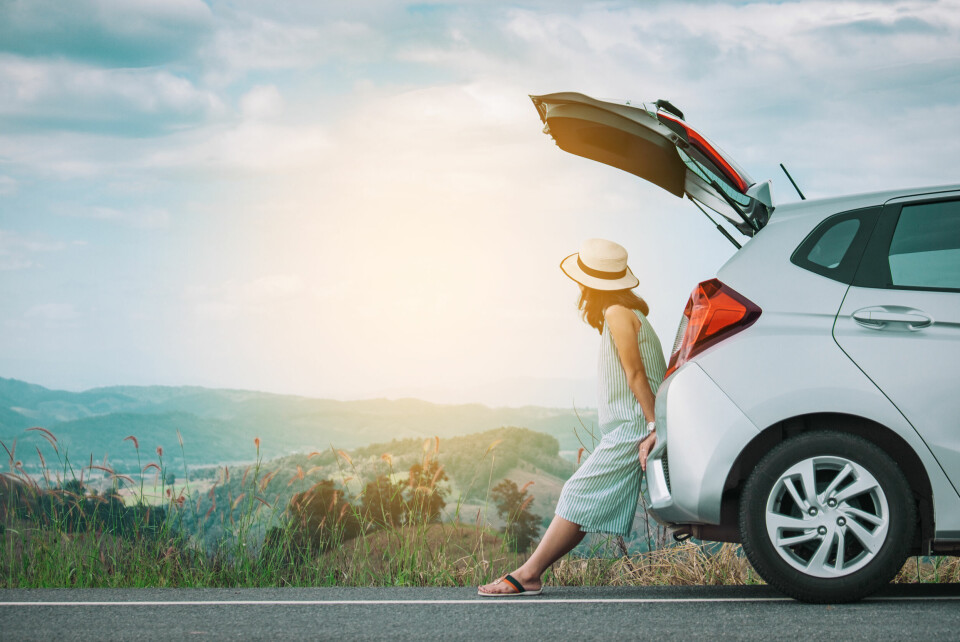 A woman in holiday wear leans on a car while looking at a beautiful view