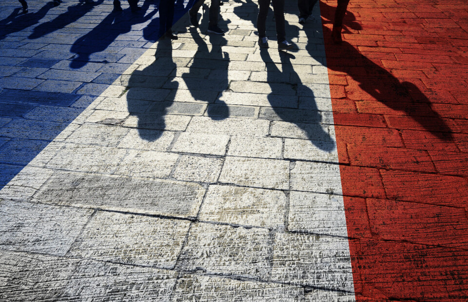A photo of shadows of people walking on a road coloured in a French tricolore flag