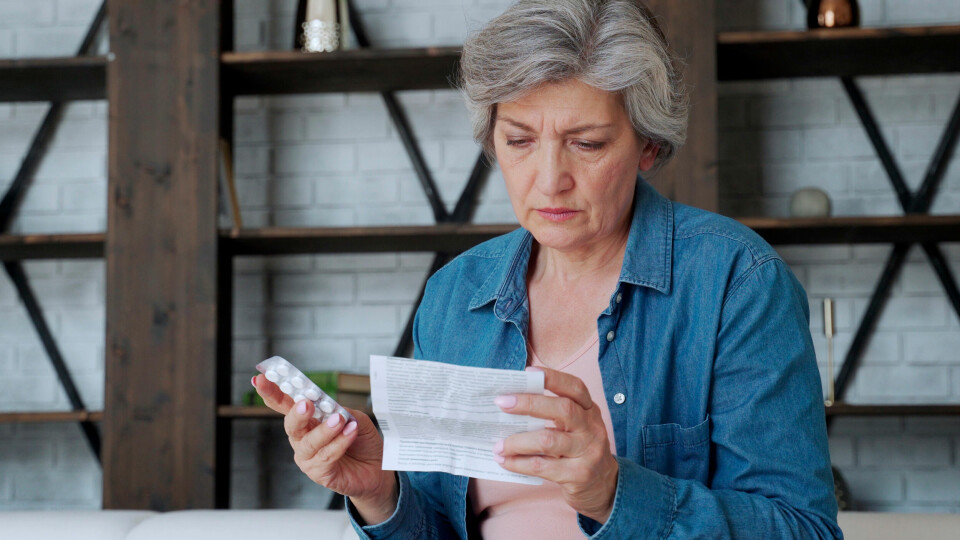 A woman holding tablets and frowning at a prescription paper