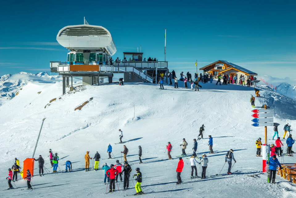 A ski station panorama showing people skiing and on chair lifts over snow covered ground and trees