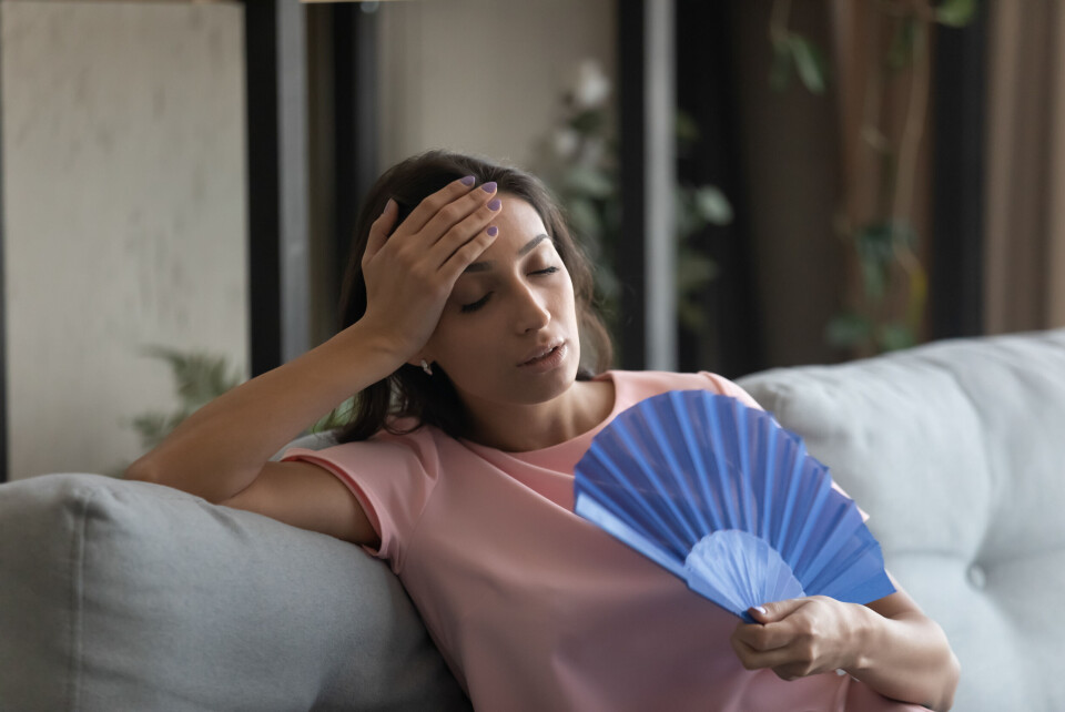 A photo of a woman sitting on a sofa fanning herself due to heat