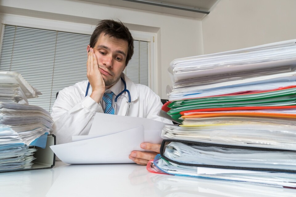 A photo of a doctor at a desk looking stressed by the amount of paperwork