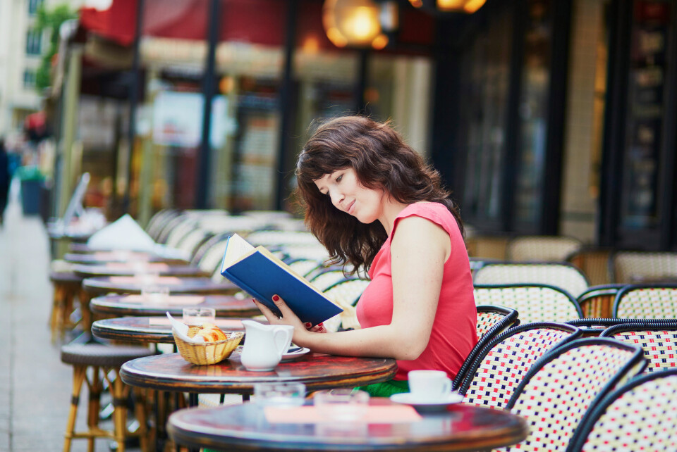 A woman sits and reads a book in a typically-French cafe