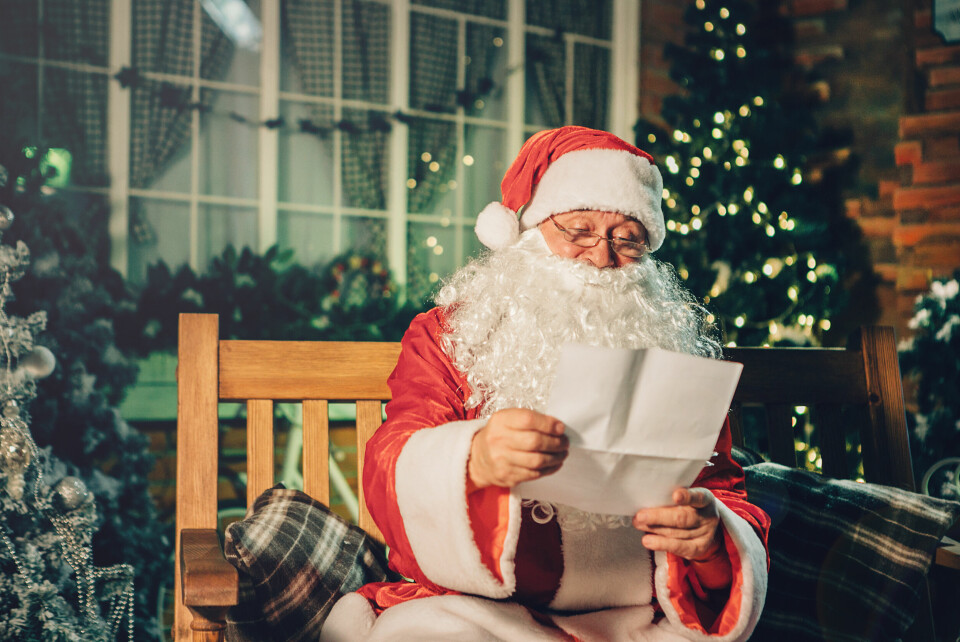 A photo of a man dressed as Father Christmas reading a letter in a decorated house