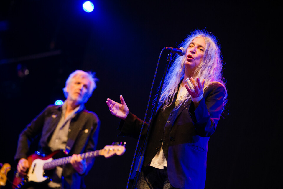 Singer Patti Smith standing on stage wearing her signature black jacket, and long grey hair