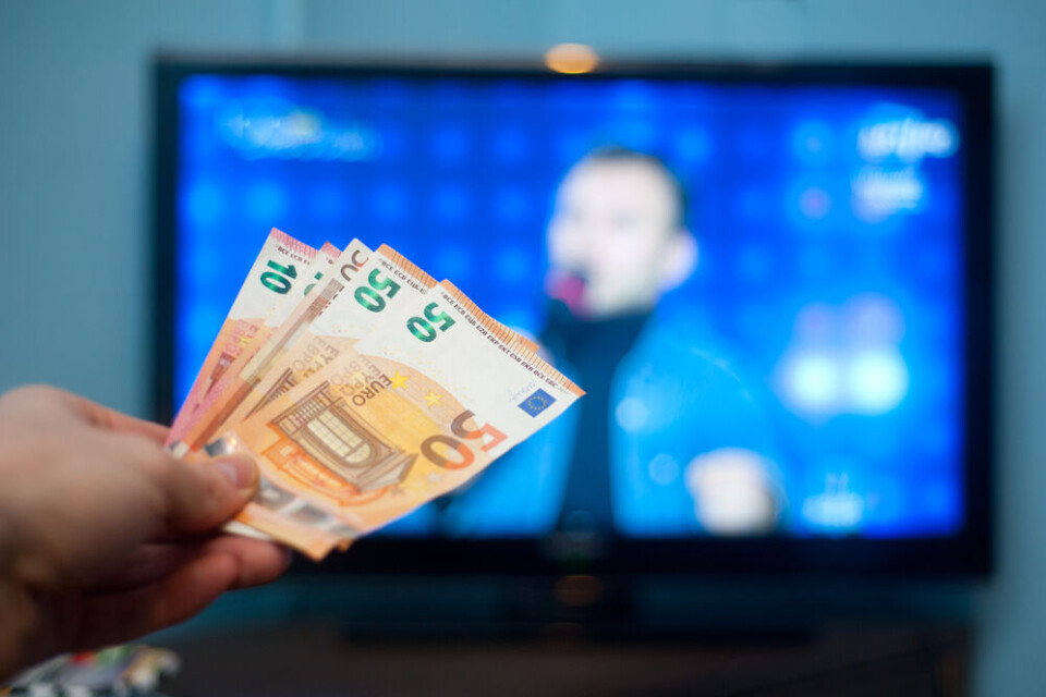 Someone holding up money in front of a TV to symobilse the licence fee