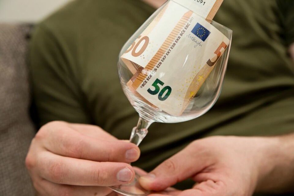 A view of a man holding a wine glass with euro notes inside