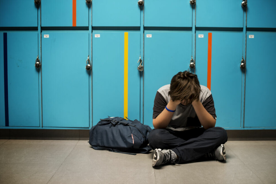 A boy sitting with his head in his hands in front of school lockers