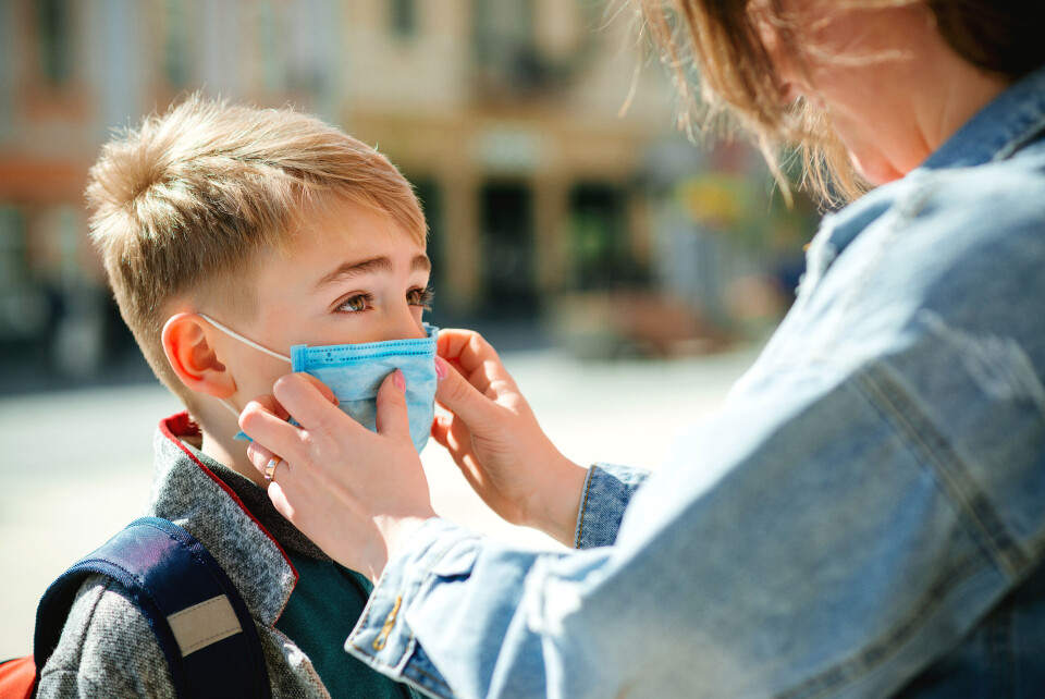 A parent puts a mask on a young child who is going to school with his rucksack.