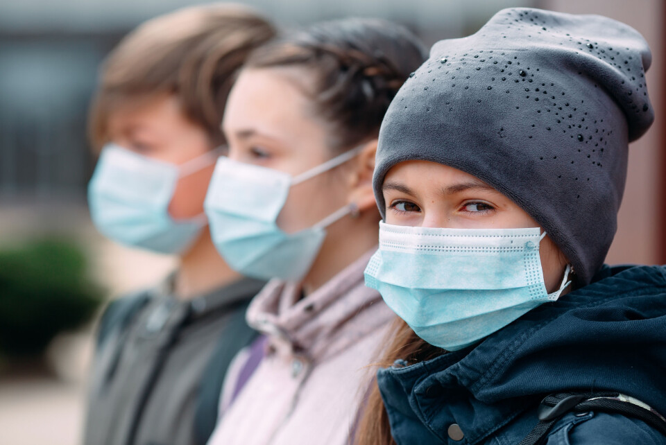 Children wearing facemasks line up, one looks at the camera