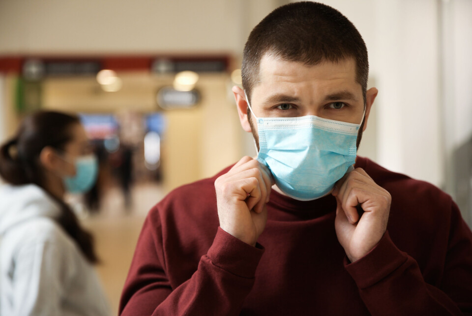 New Africa / Shutterstock A man adjusting a disposable mask on his face while indoors