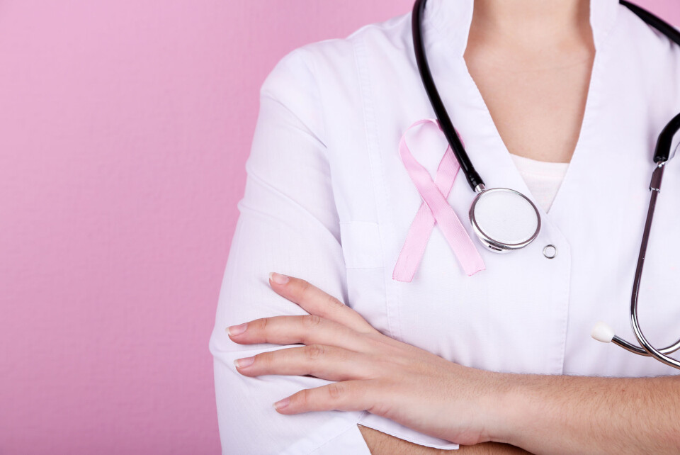 Doctor with stethoscope around her neck and pink breast cancer awareness ribbon pinned to white coat