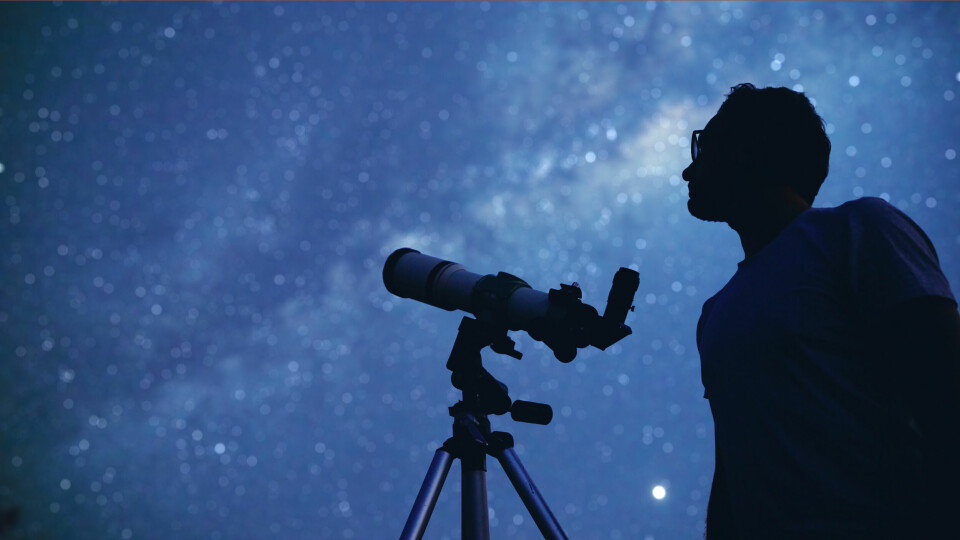 Astronomer looking up at the night sky with telescope