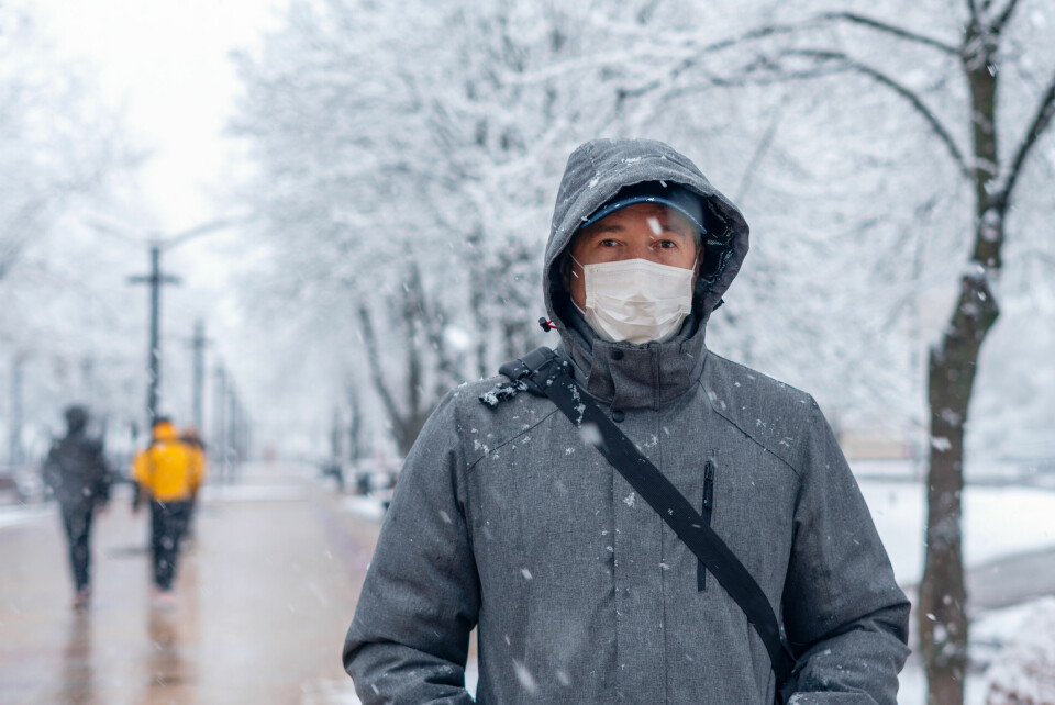 A man wearing a thick coat and a face mask outdoors in snow