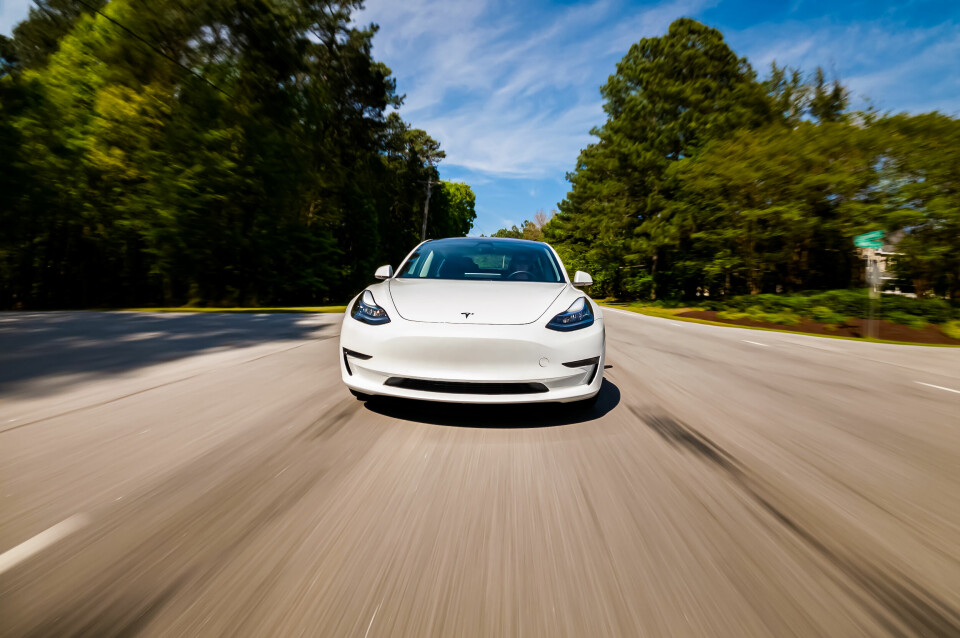 A Tesla Model 3 electric vehicle driving fast down a road