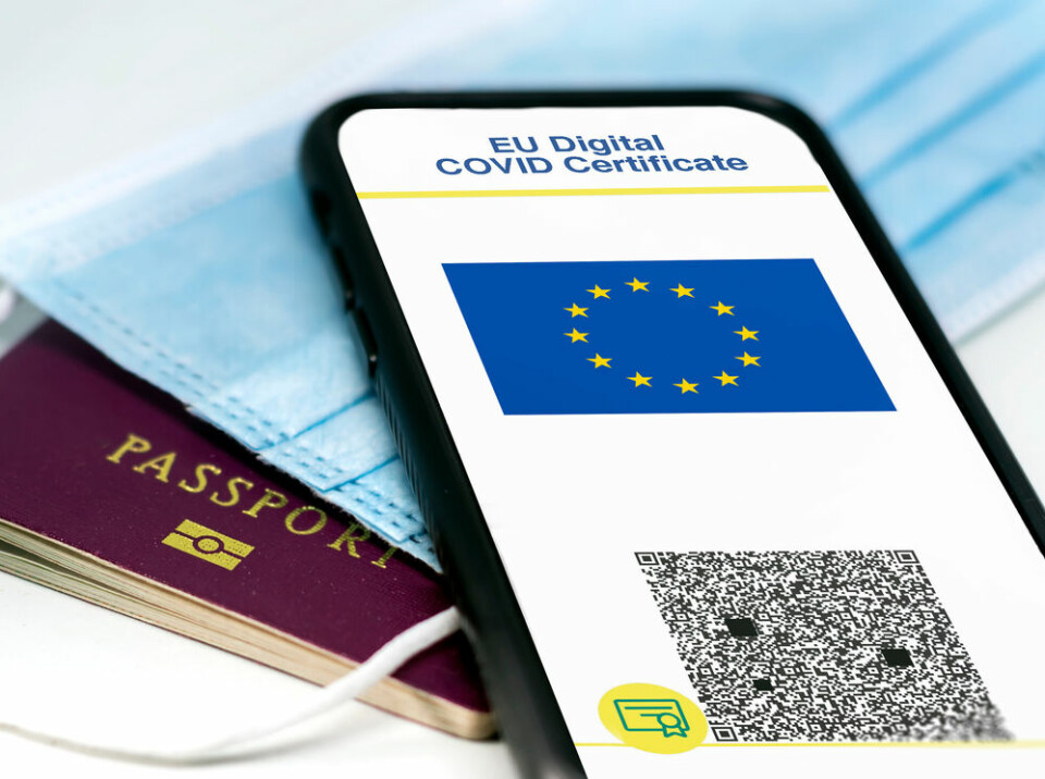 EU Digital COVID Certificate with the QR code on the screen of a mobile phone over a surgical mask and a passport.