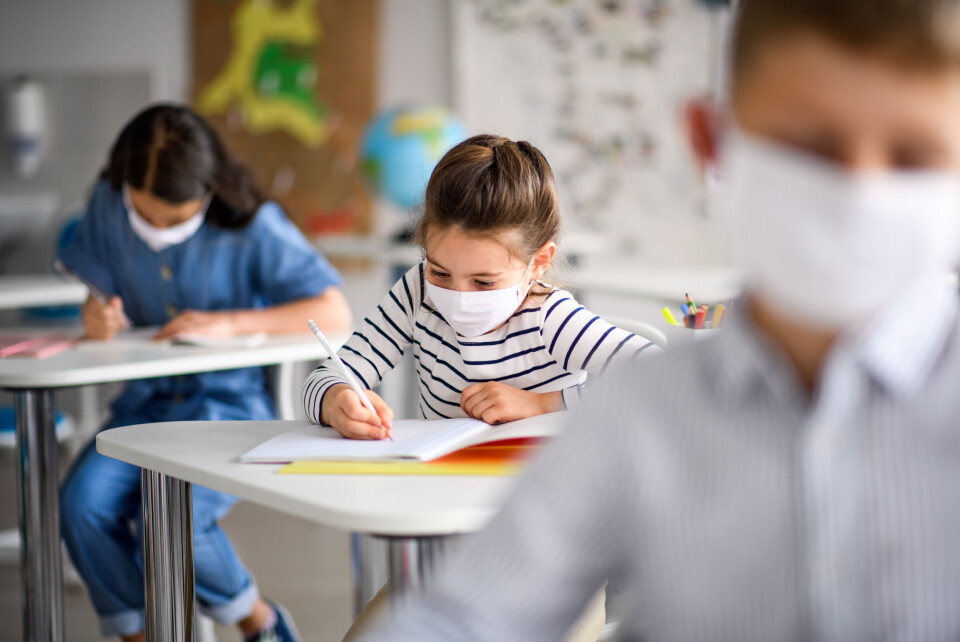 Halfpoint / Shutterstock An image of three young children in a classroom sitting at desks with their masks on
