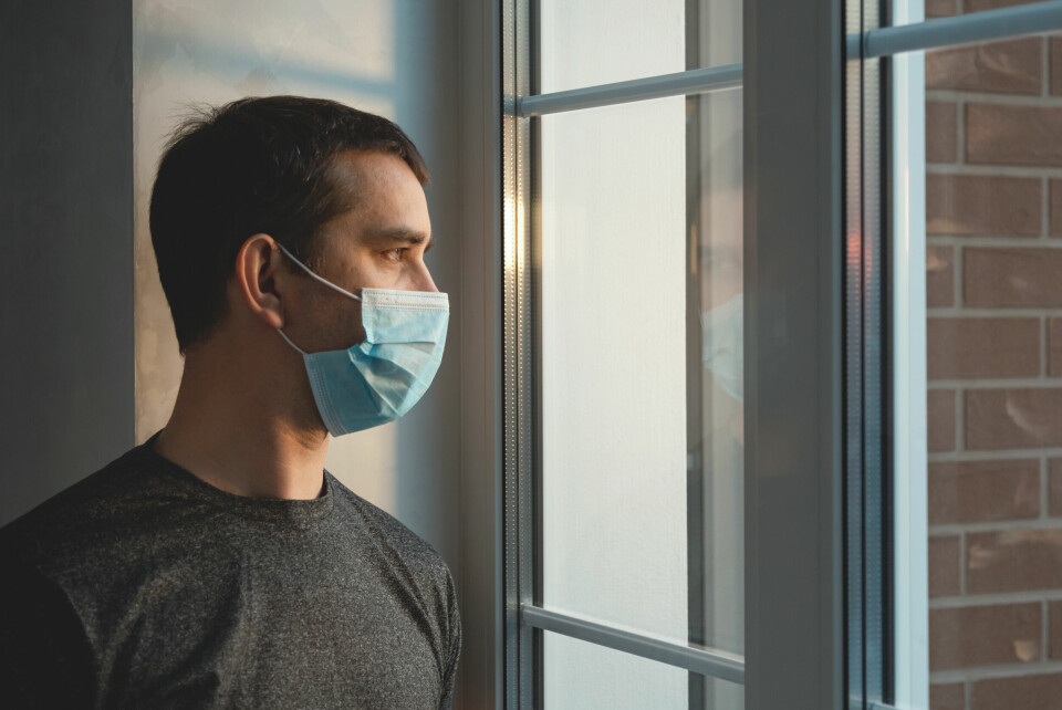 An image of a man in quarantine, wearing a mask and looking out of the window