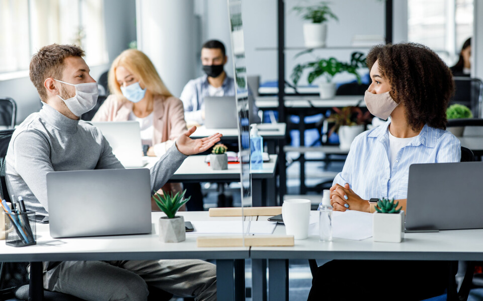 Colleagues chat while wearing masks in an office workspace