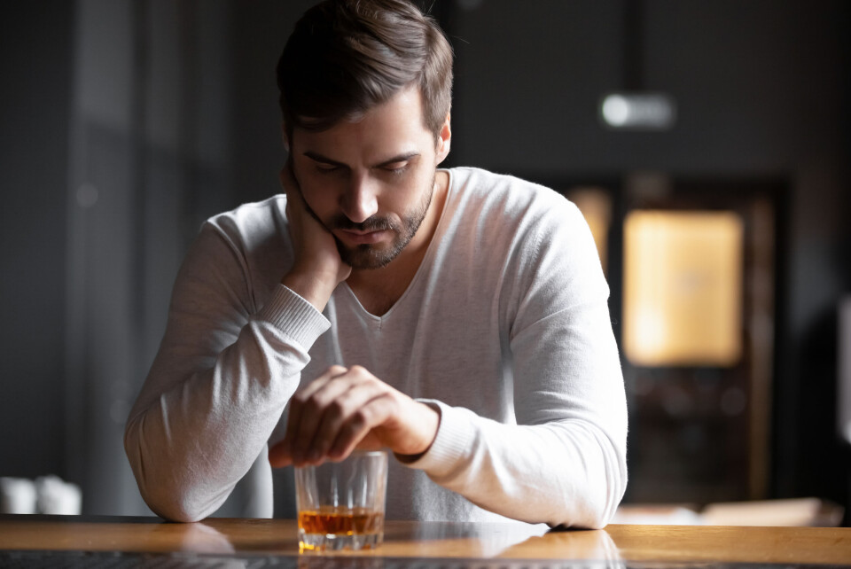 A man looking fed up with a drink in front of him