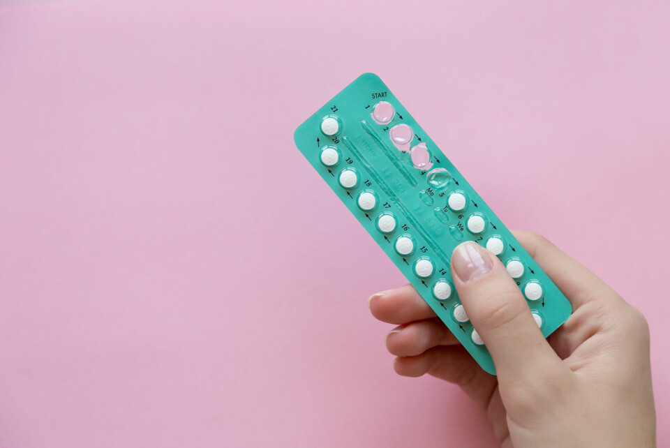 A woman holding a turquoise pack of oral contraceptives on a pink background