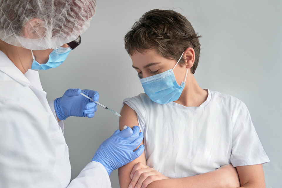 A young boy receiving a vaccination, with both nurse and boy wearing a mask