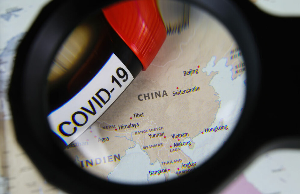 View through magnifying glass on map with focus on China and blood sample vial covid-19. French scientists join group calling for inquiry into Covid origins