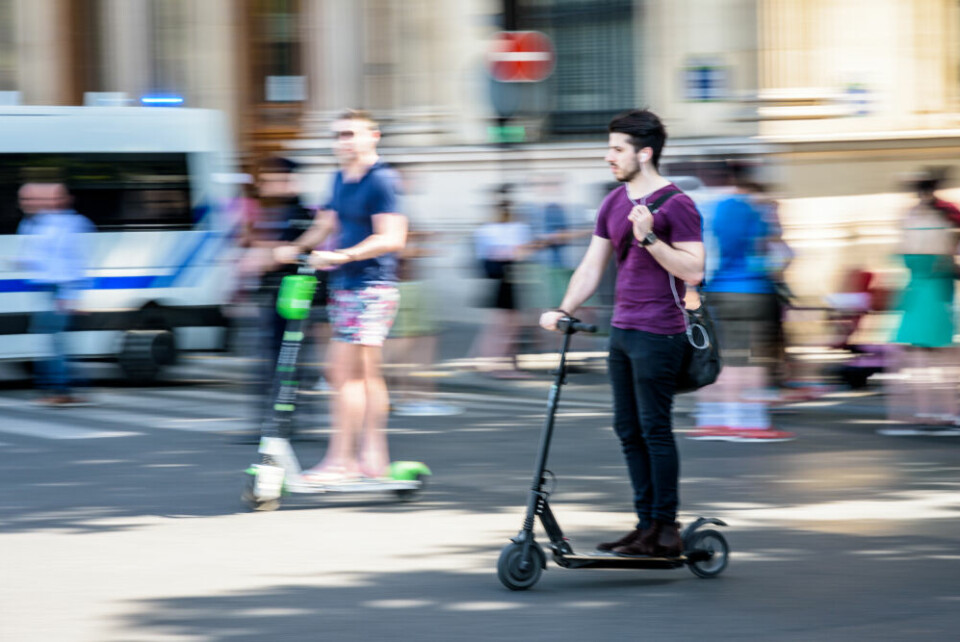 A man rides an electric scooter in Paris, with another man on another scooter behind. Electric scooters temporarily banned from Champs-Elysées
