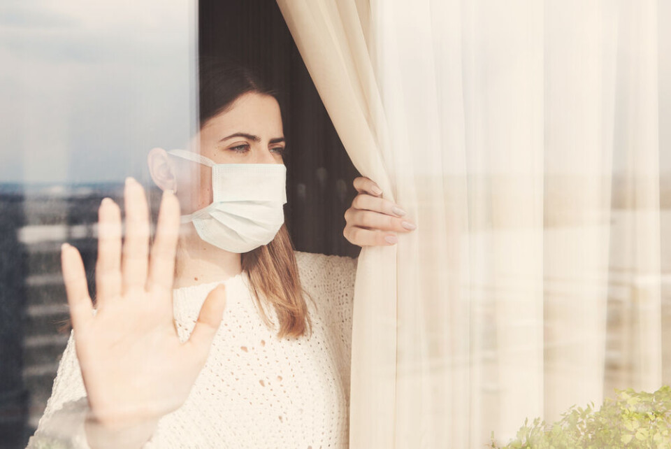 Liudmyla Guniavaia / Shutterstock Woman wearing mask looks outside and holds hand up to window in isolation. Why France will not enforce 10-day isolation after positive Covid test