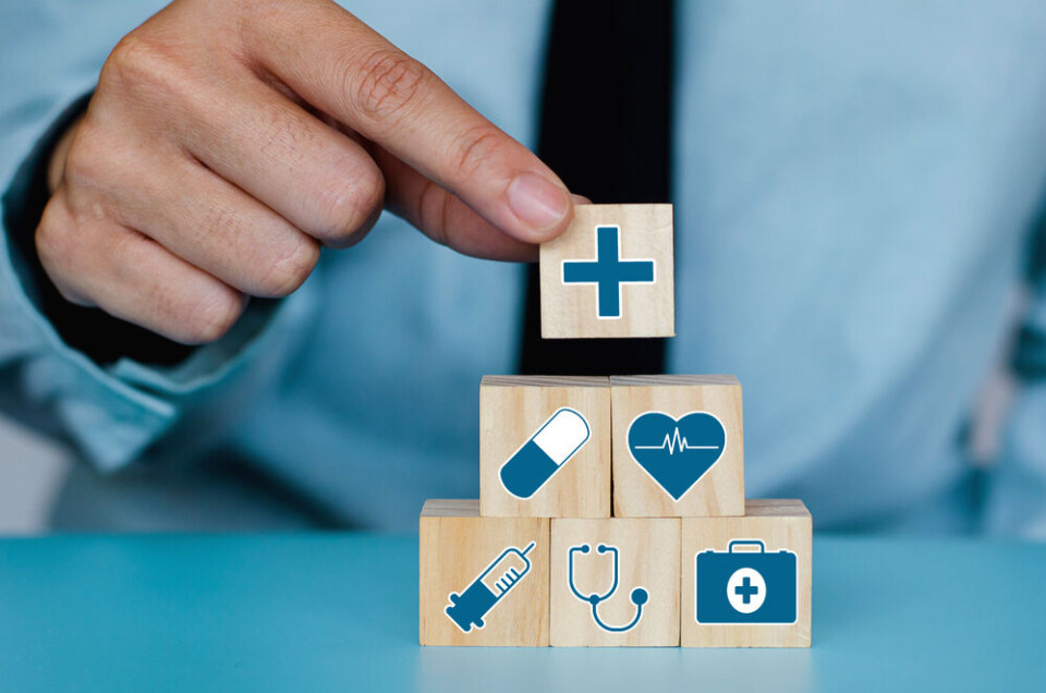 A man placing a block on top of a pyramid of blocks with healthcare symbols on them