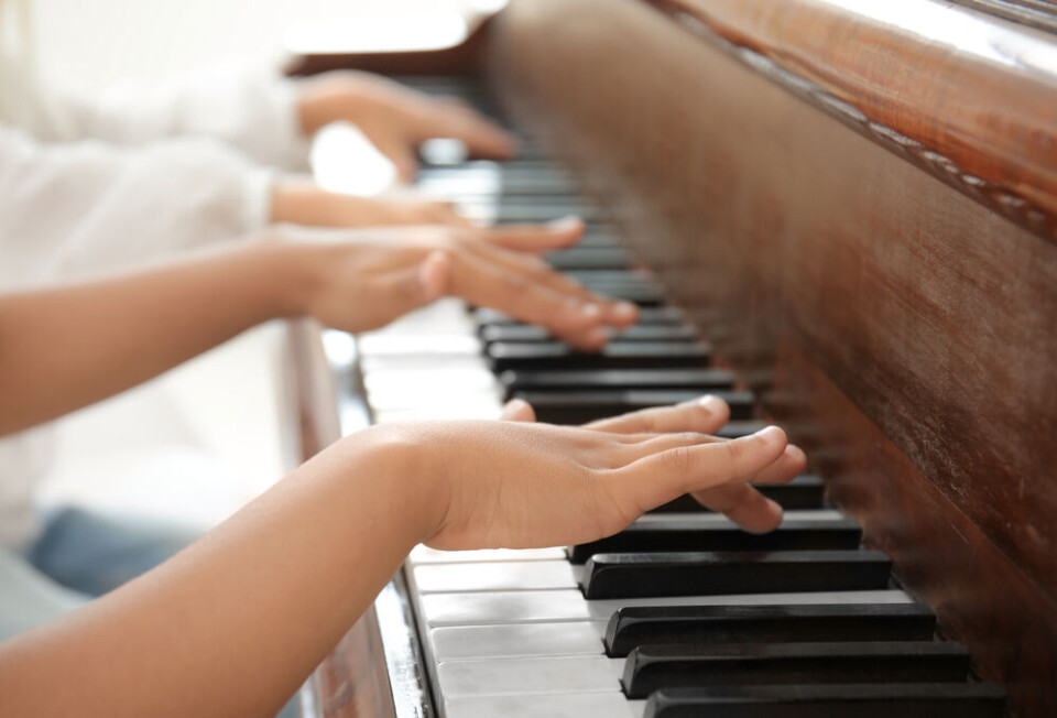 A child playing piano with the help of an adult teacher