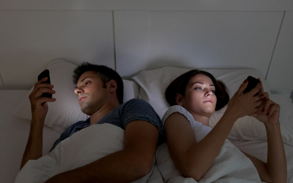 A couple in bed each looking at separate phones