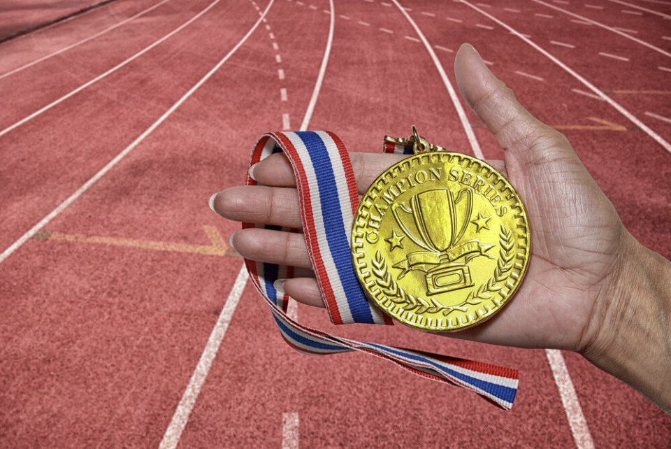 A view of a hand holding a gold medal, with a running track in the background
