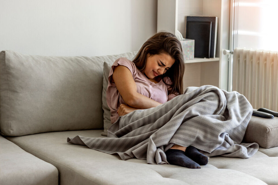 A woman curled up in pain under a blanket on a sofa