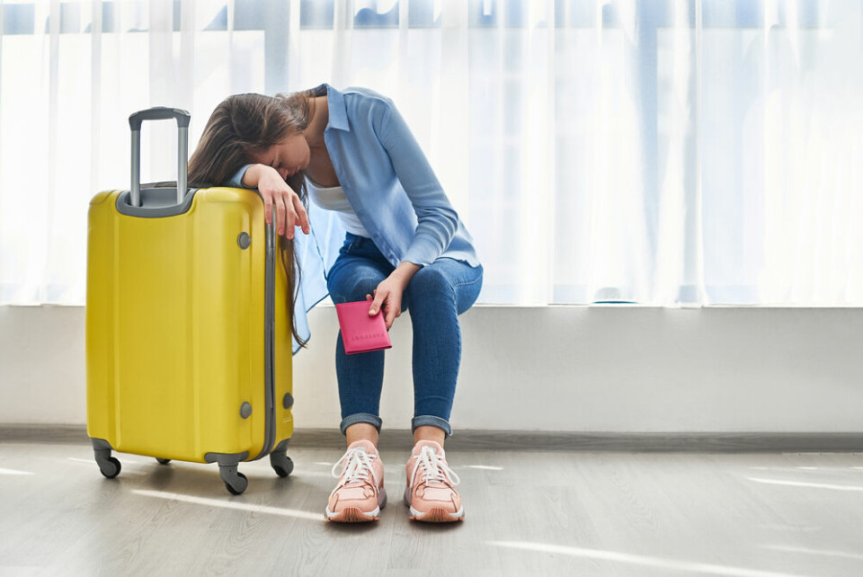A woman looking fed up, with her head on her yellow suitcase, to show travel problems