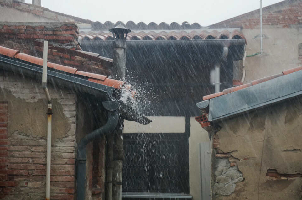 Rainwater overflowing from the tiled roofs and gutters of an old brick house in France