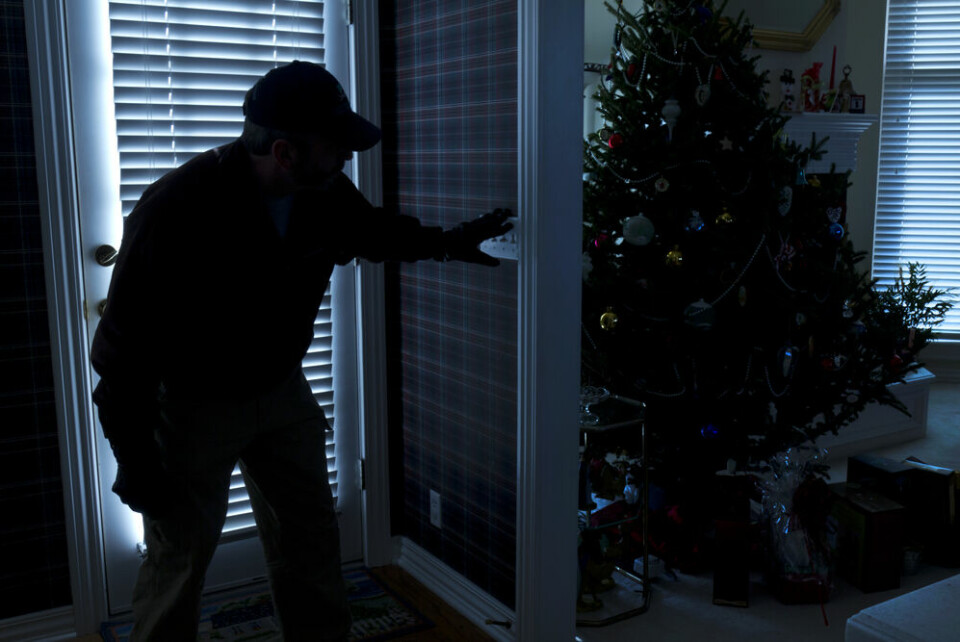 A view of a man dressed in black, sneaking into a dark house that has a Christmas tree up