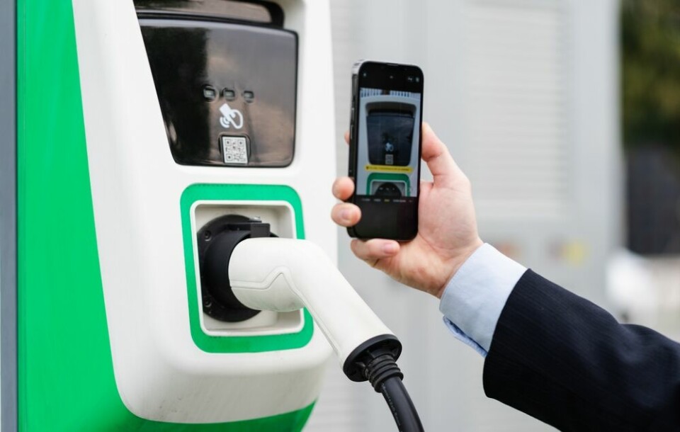 A man holding up his smartphone to a QR code on an electric car charging station