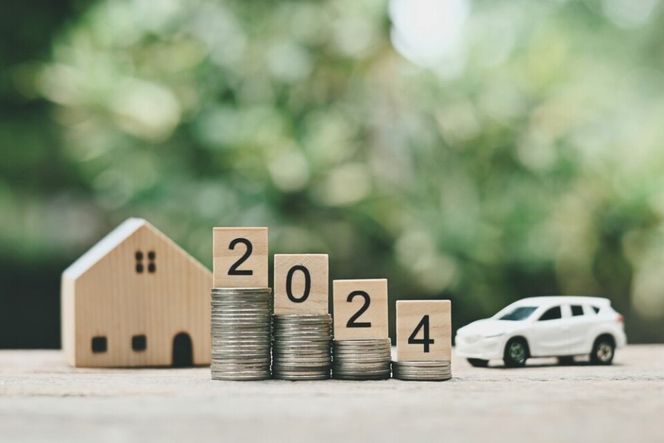 A view of a model house and car, with the numbers 2024 on top of coins to show a rise in insurance premiums for next year