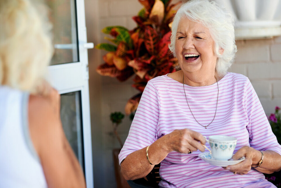 A view of an older woman drinking a cup of tea and laughing