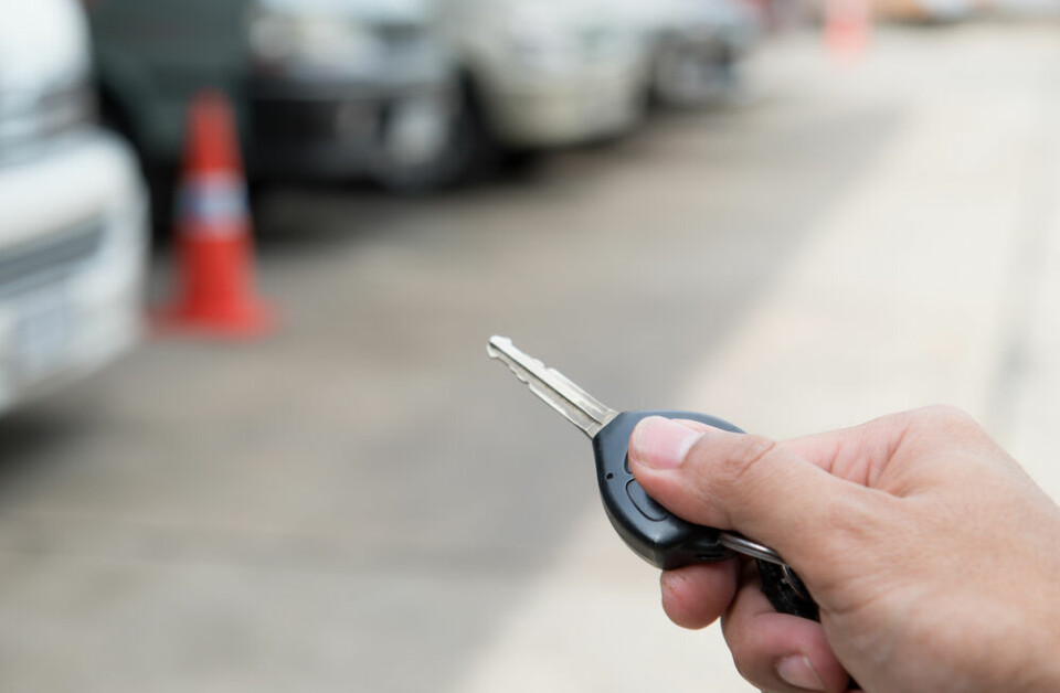 A man holding a new vehicle key against a backdrop of vehicles at a garage